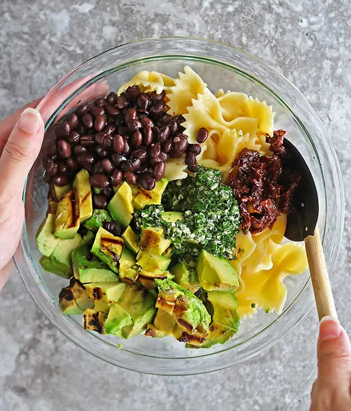 Overhead photo of a hand mixing together the ingredients to make this healthy pasta salad.