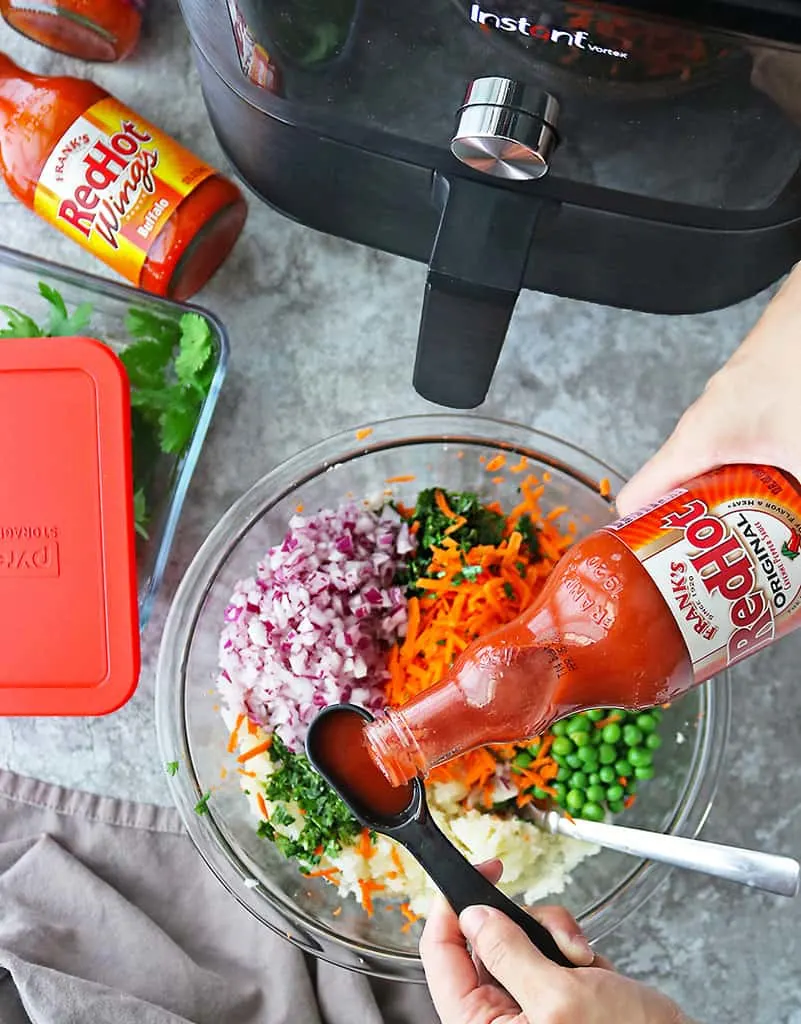 Photo showing the addition of Franks RedHot to the ingredients to make spicy veggie fritters.