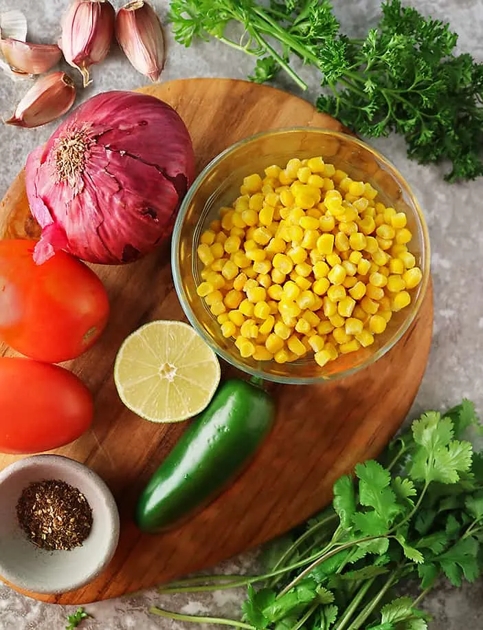 ingredients to make corn salad laid on a cutting board boarded with cilantro and parsley