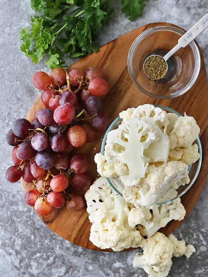 Ingredients to make roasted cauliflower and grapes on a wooden cutting tray.