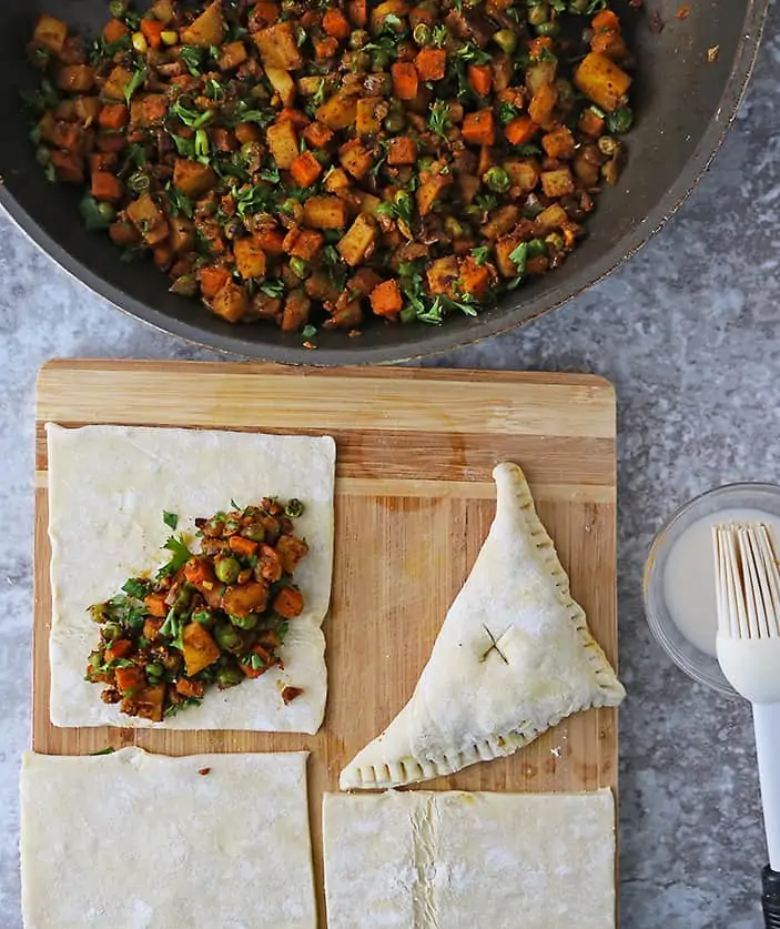 Placing the veggie stuffing into puff pastry squares and folding them over to make veggie stuffed puff pastry triangles