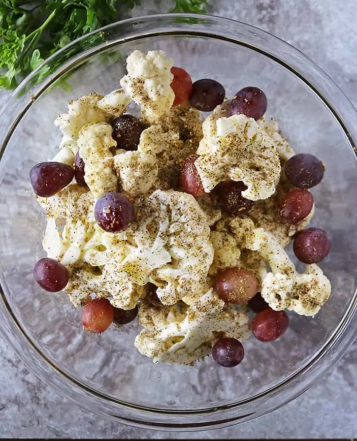 mixing together grapes and cauliflower with oil and zaatar before baking.