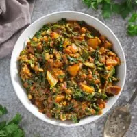 A big bowl of easy kale curry with potatoes on a gray background.