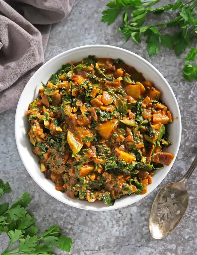 A big bowl of easy kale curry with potatoes on a gray background.
