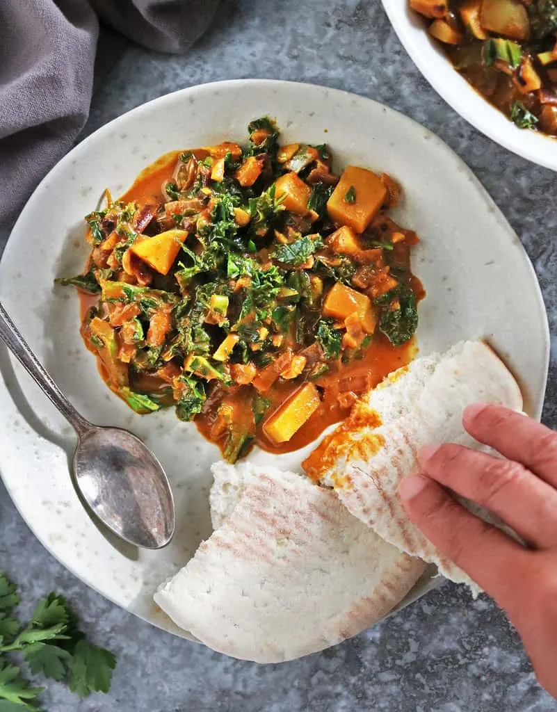 Digging into a plate of kale curry with pita bread