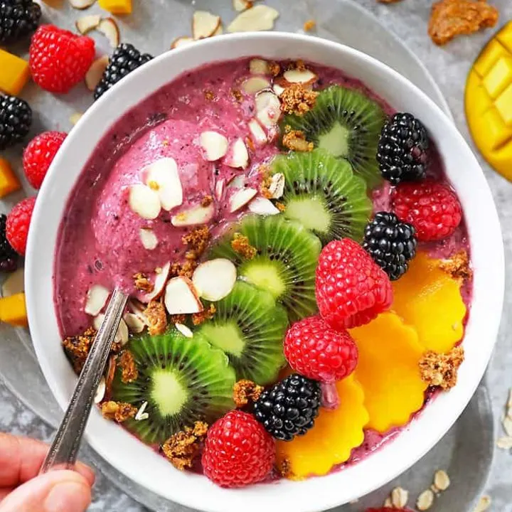 Waken up your senses with this delicious plant based Berry Oatmeal Smoothie Bowl in a white bowl on a grey background. Oatmeal smoothie bowl is topped with mango, kiwi and berries.