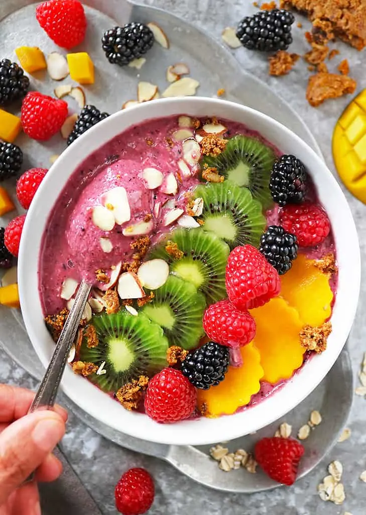 Waken up your senses with this delicious plant based Berry Oatmeal Smoothie Bowl in a white bowl on a grey background. Oatmeal smoothie bowl is topped with mango, kiwi and berries.