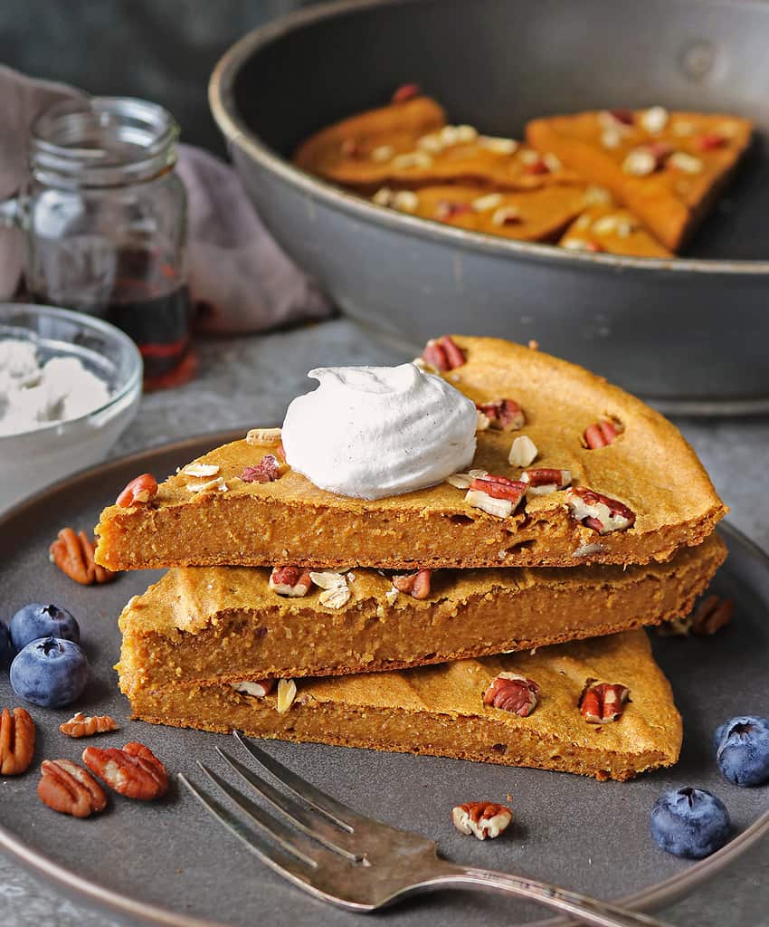 Slices of Easy gluten-free and refined sugar-free baked oatmeal with pumpkin stacked on top of each other with dairy free whipped cream on top