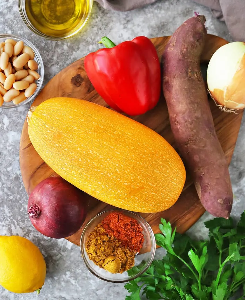 Ingredients to make sheet pan veggies and orangetti squash laid out on a gray table.