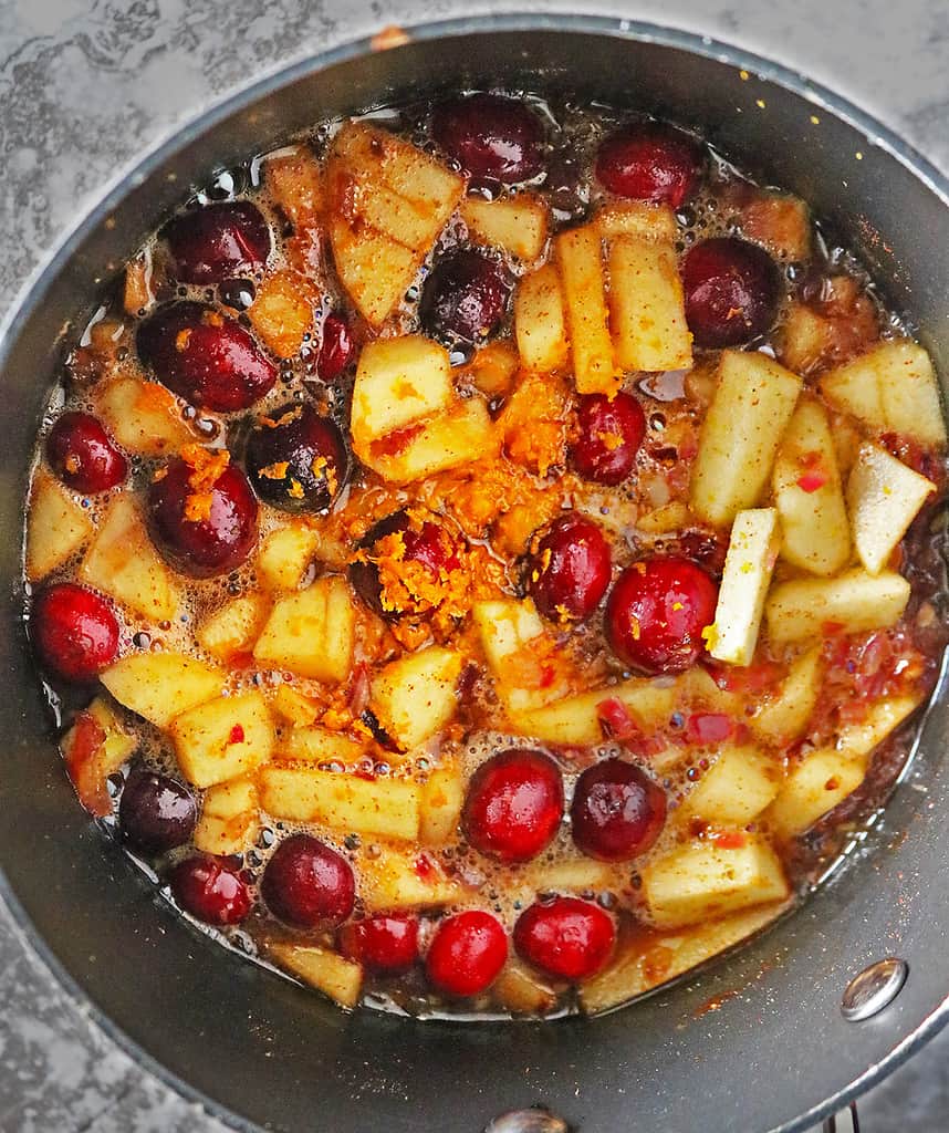 Making Cranberry Apple Chutney by simmering all the ingredients together in a large pot.