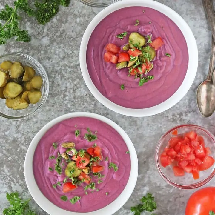 Thick creamy purple sweet potato soup in two large white bowls with toppings.