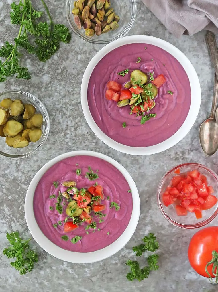 Thick creamy purple sweet potato soup in two large white bowls with toppings.