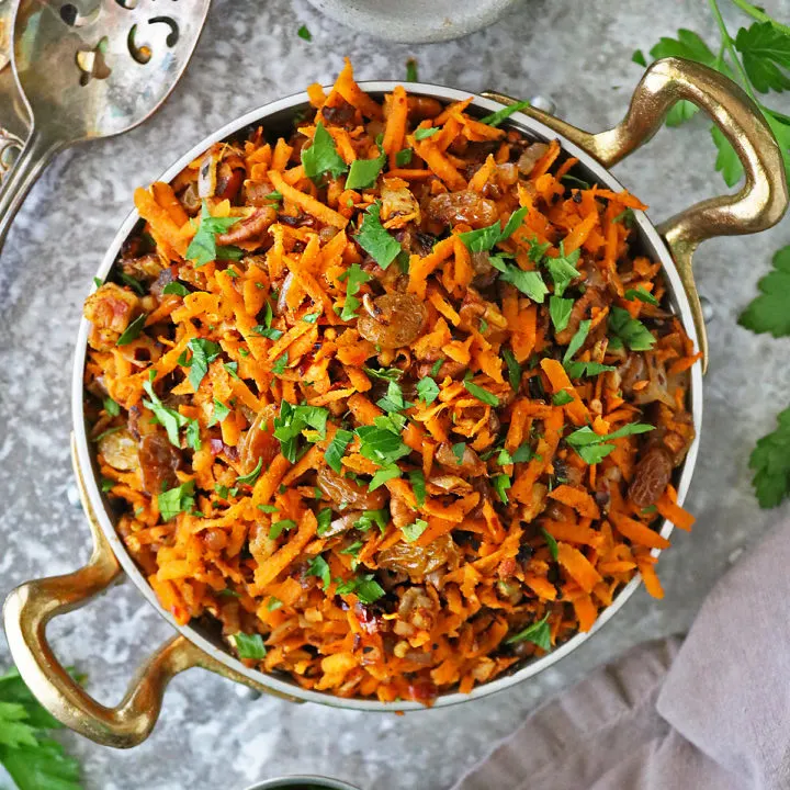 Easy healthy carrot raisin salad in a gold skillet with parsley and chili flakes around.