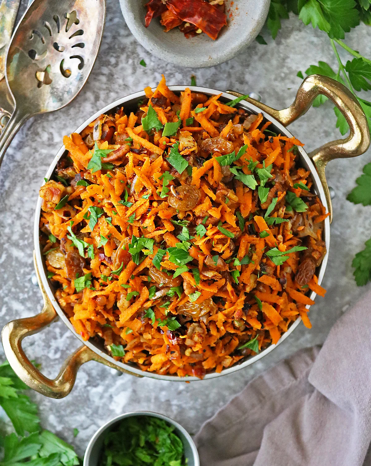 Easy healthy carrot raisin salad in a gold skillet with parsley and chili flakes around.