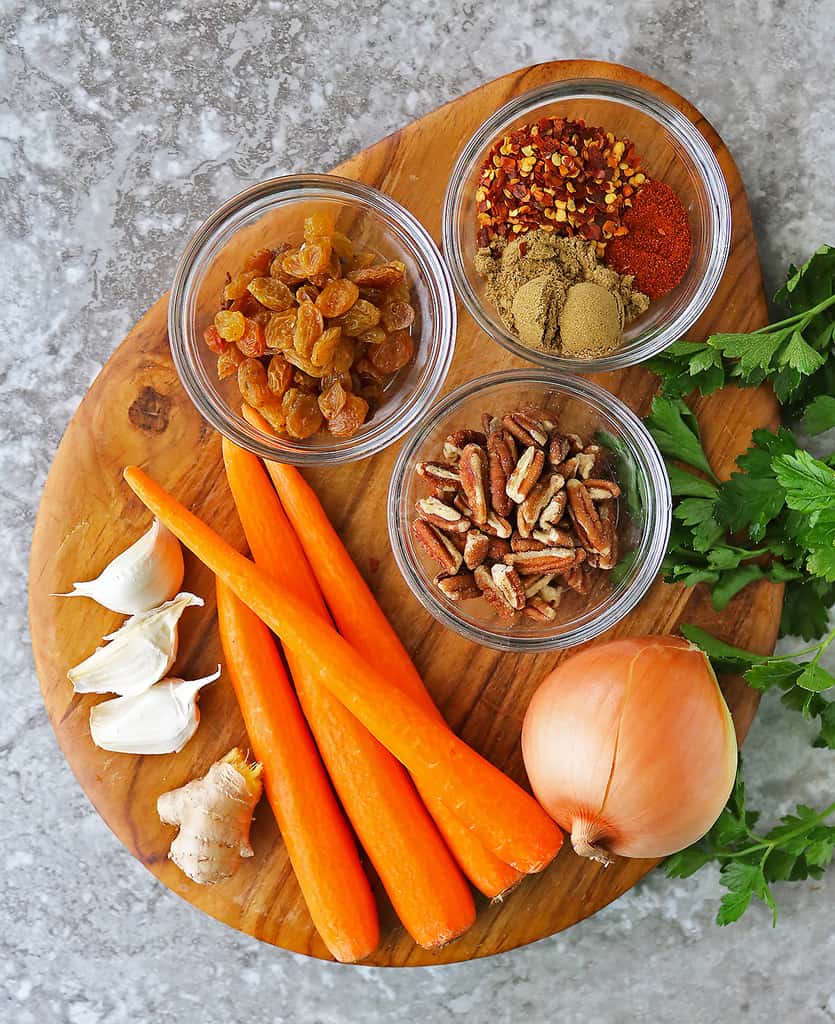 The 10 Ingredients to make sweet spicy carrot raisin salad on a board.