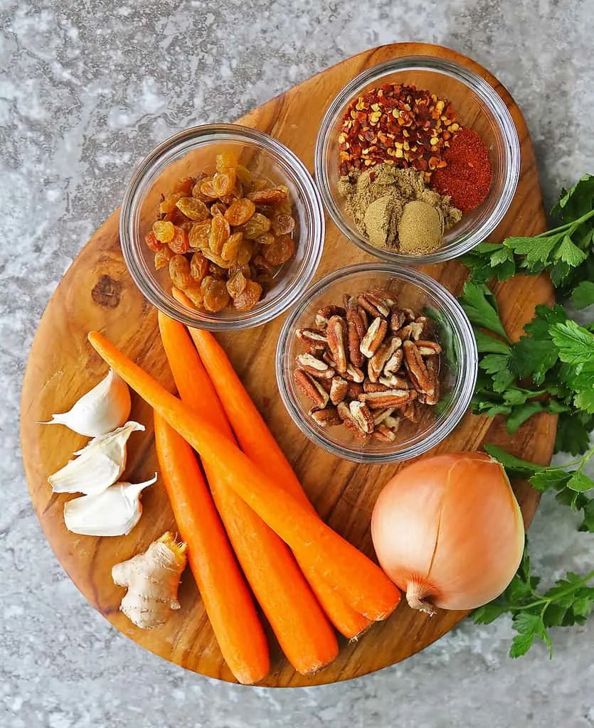 The 10 Ingredients to make sweet spicy carrot raisin salad on a board.