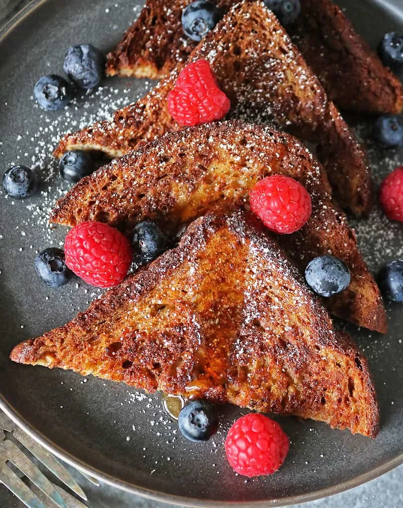 The best Vegan French toast on a gray plate with maple syrup drizzled on it.