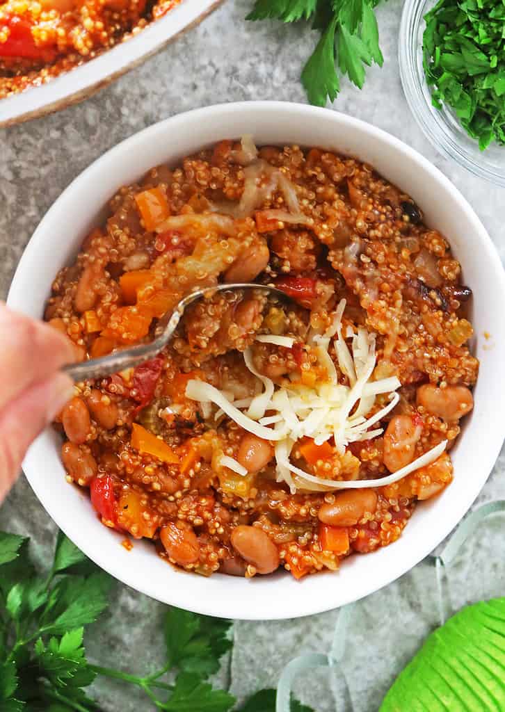 Adding cheese to bowl of vegetarian quinoa with enchilada sauce
