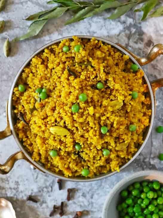 Turmeric quinoa in a gold pan with cardamom pods and cloves scattered around.