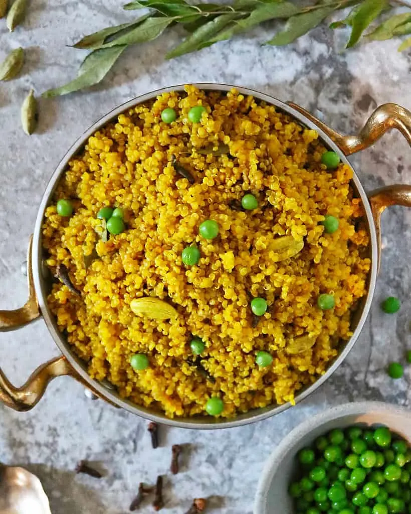 Turmeric quinoa in a gold pan with cardamom pods and cloves scattered around.