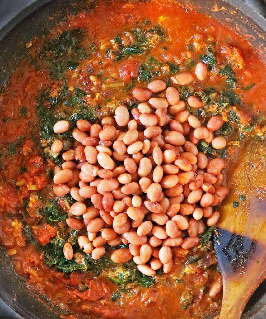 Adding pinto beans to a rich tomato broth in a pan.