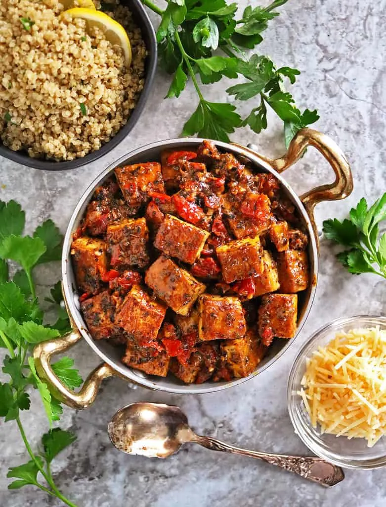 Tofu in flavorful coconut cream sauce with sundried tomatoes served in a gold rimmed pan.