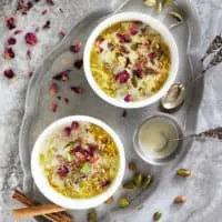 Dairy-free Gluten-free Oat kheer or Oat pudding in two white bowls with rose petals and pistachios scattered around.