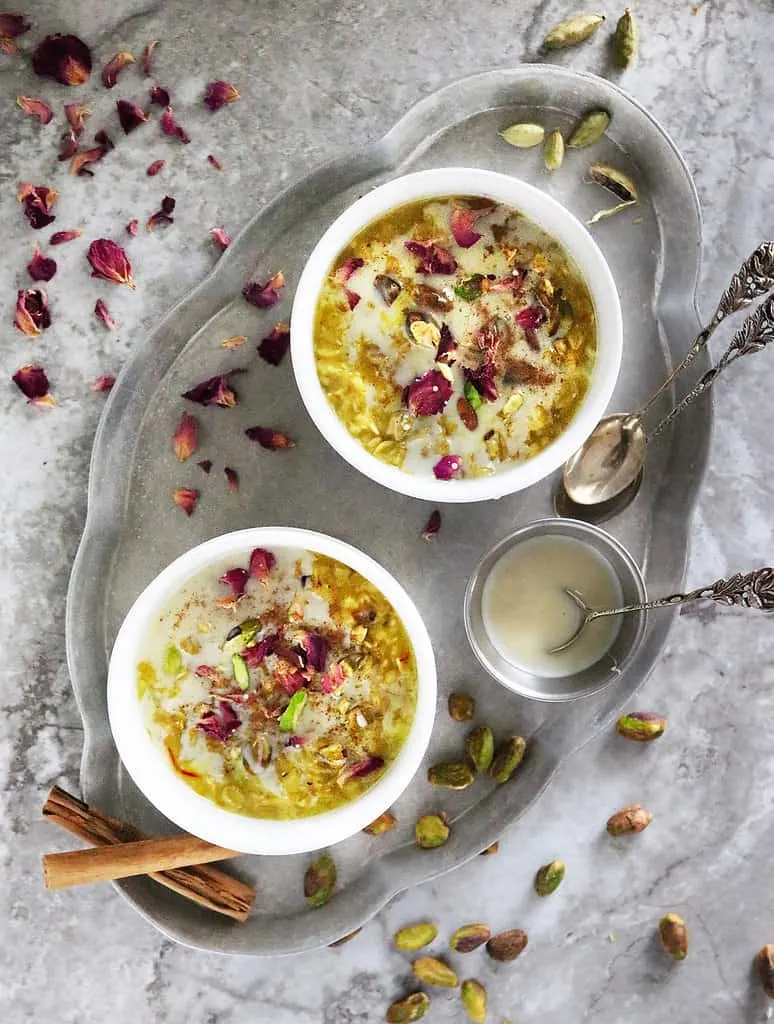 Dairy-free Gluten-free Oat kheer or Oat pudding in two white bowls with rose petals and pistachios scattered around.