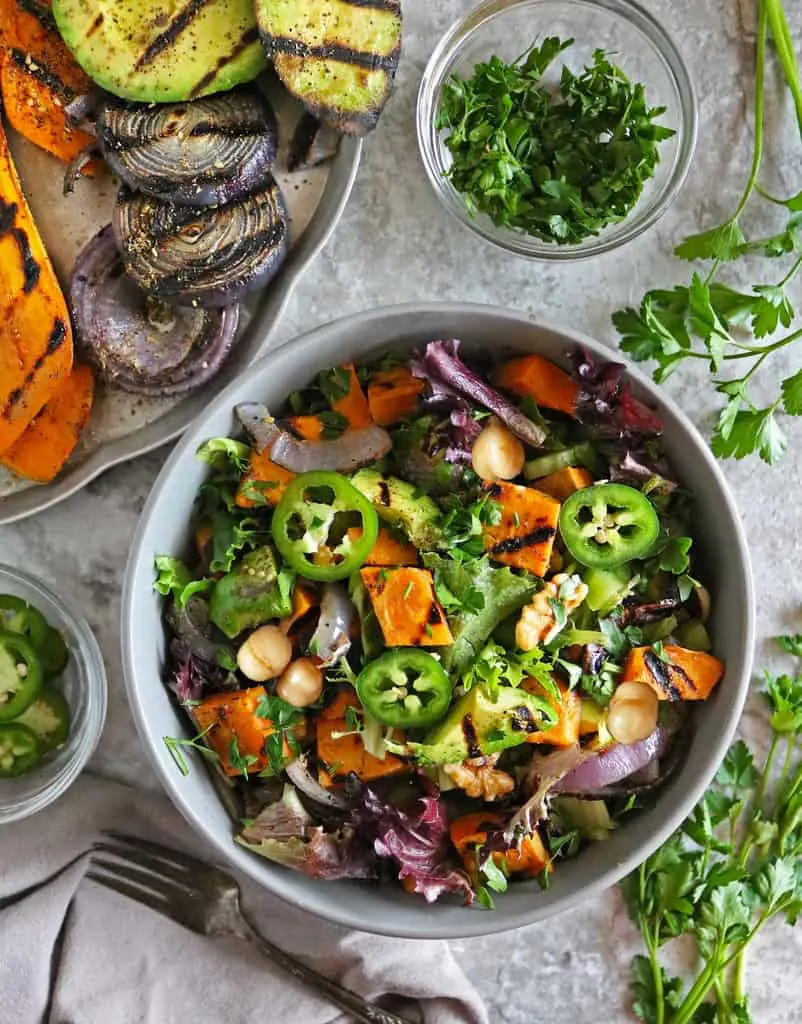 A bowl with a healthy sweet potato summer salad along with grilled sweet potato, grilled avocado, and grilled onions on a tray.