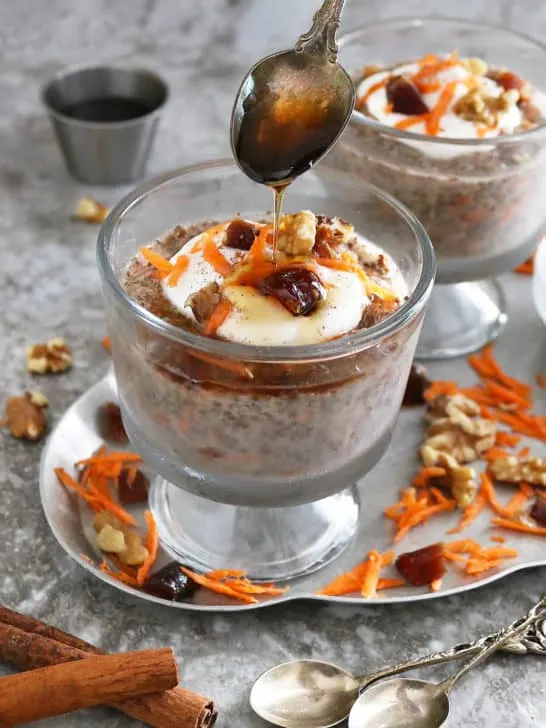 carrot cake chia pudding in a bowl, topped with yogurt, dates, walnuts, cinnamon, and maple syrup