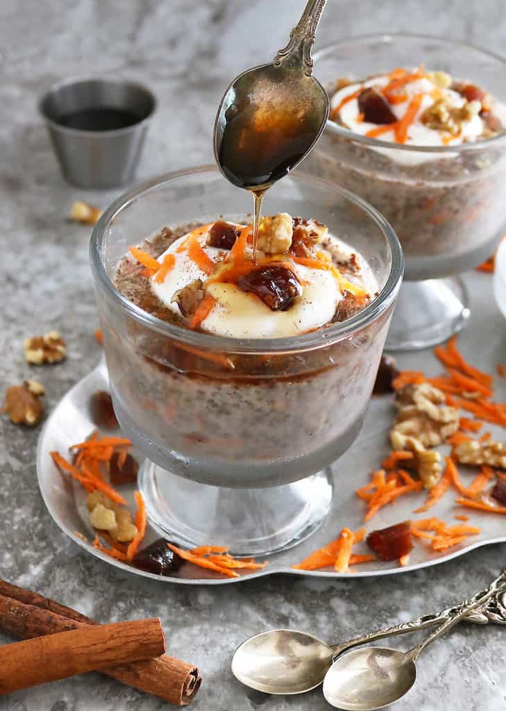 carrot cake chia pudding in a bowl, topped with yogurt, dates, walnuts, cinnamon, and maple syrup