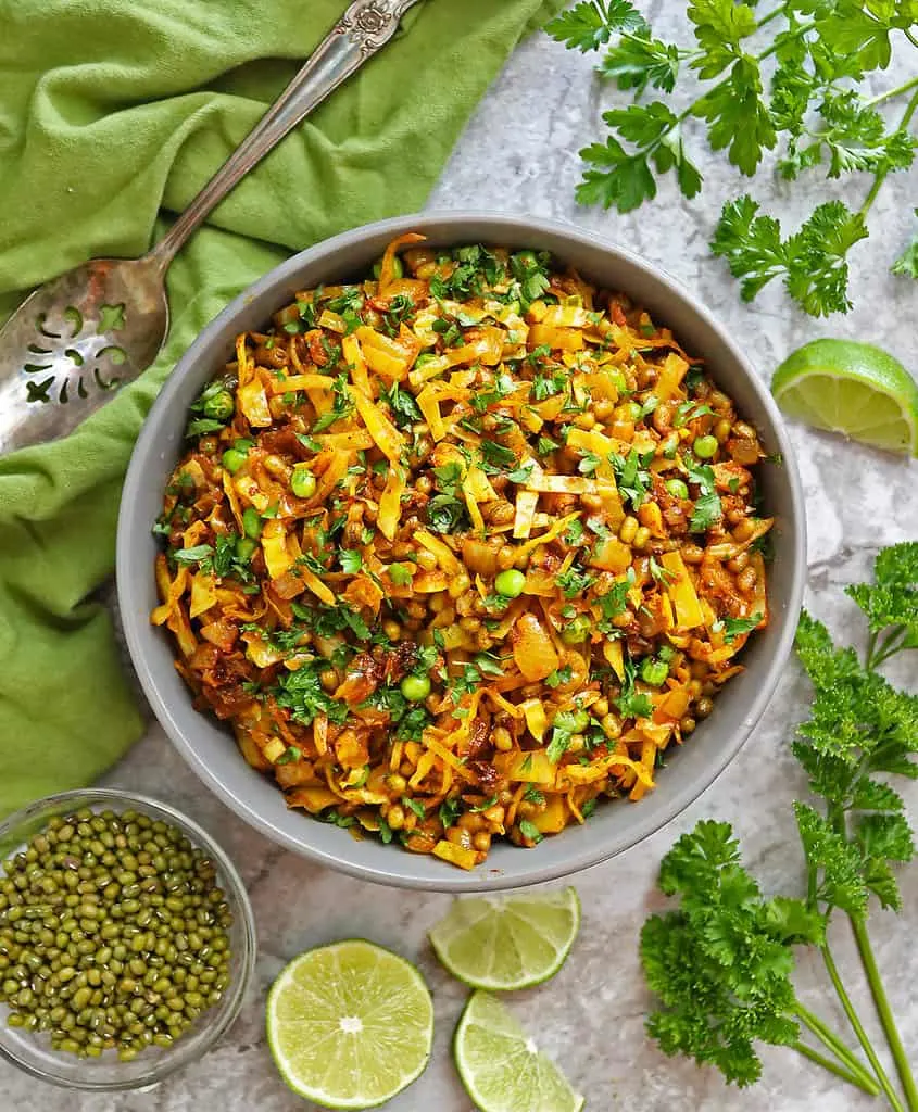 Mung Bean Cabbage Sauté in a gray bowl with parsley, mung beans, and lime surrounding it.