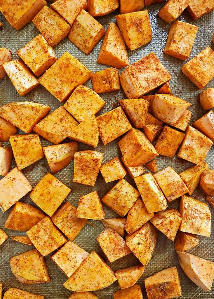 Spiced sweet potatoes on a baking tray, ready to be oven roasted to perfection.