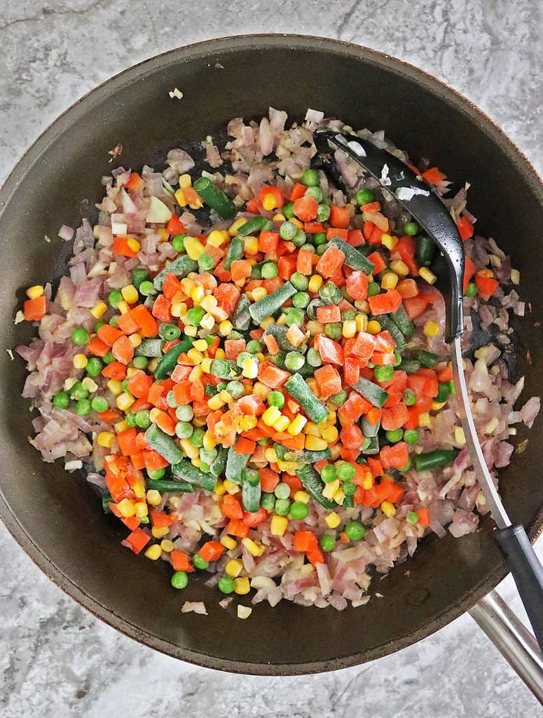 Sautéing onions, ginger, garlic with frozen veggies and spices in a large pan.