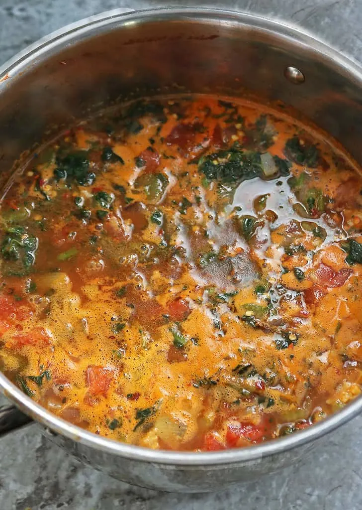 Simmering spices chicken veggies tomatoes in chicken stock to make lasagna soup.