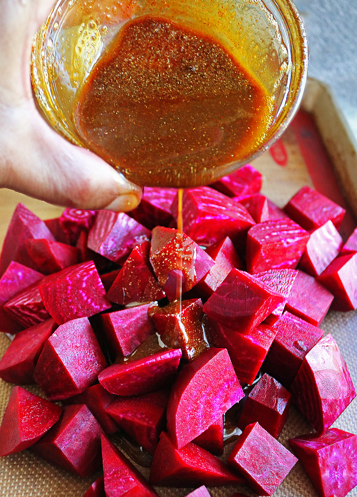 Pouring spiced oil on to cut up beetroot before tossing them to coat them well.