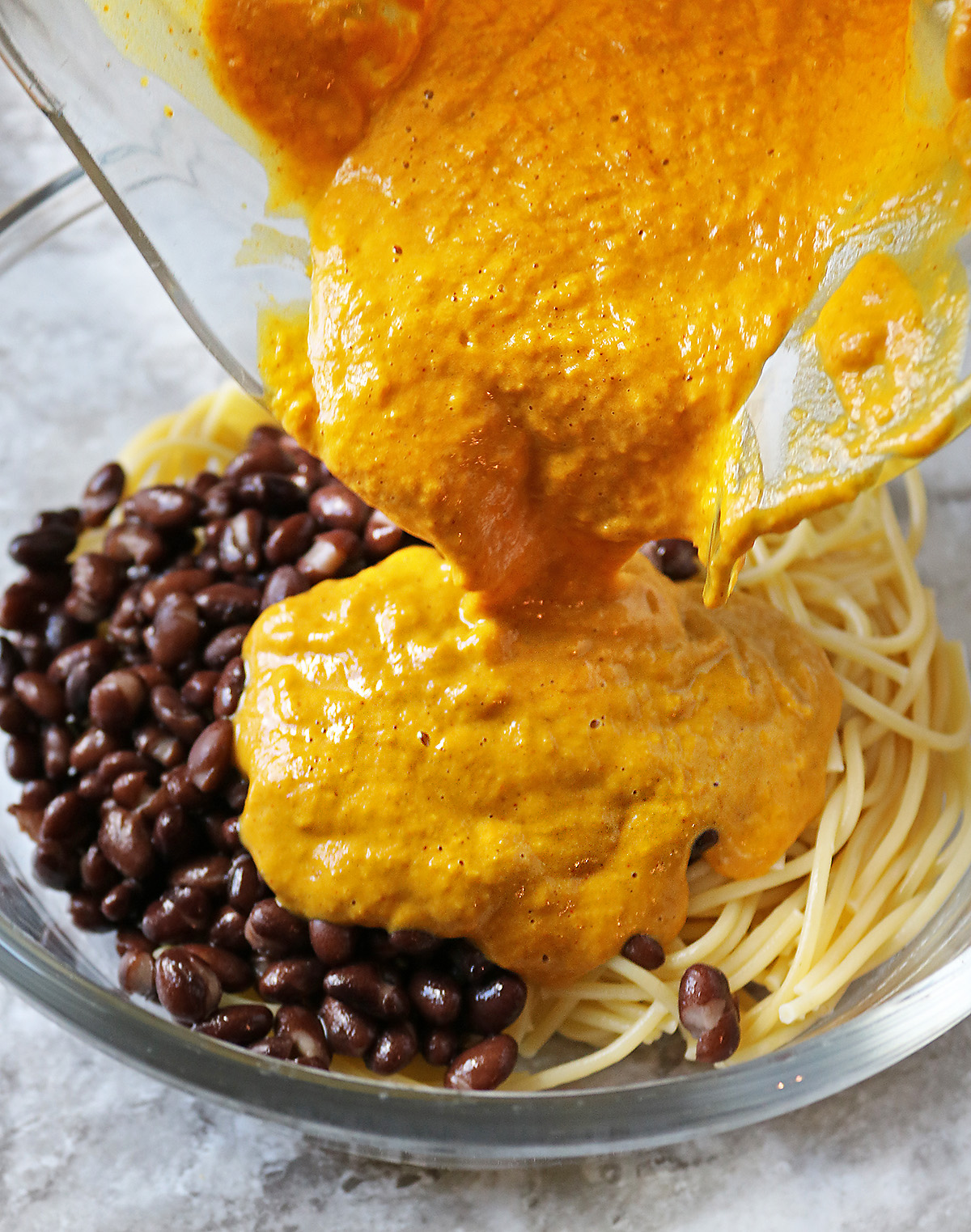 Pouring dairy free pumpkin cream sauce onto spaghetti and beans