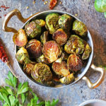 My favorite Oven Roasted Brussels sprouts with Berbere in a golden skillet with chili flakes and cilantro garniches.