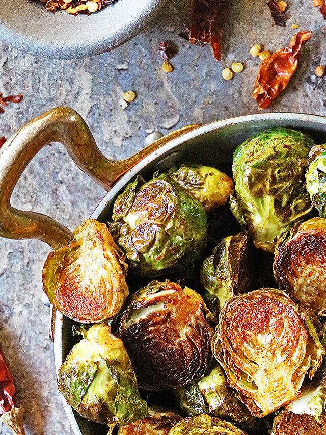 My favorite Oven Roasted Brussels sprouts with Berbere in a golden skillet with chili flakes and cilantro garniches.