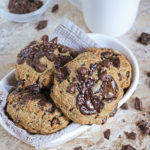 Brown Butter Rye Chocolate Chip Muffin Tops in a white bowl with a cup of coffee in the background.