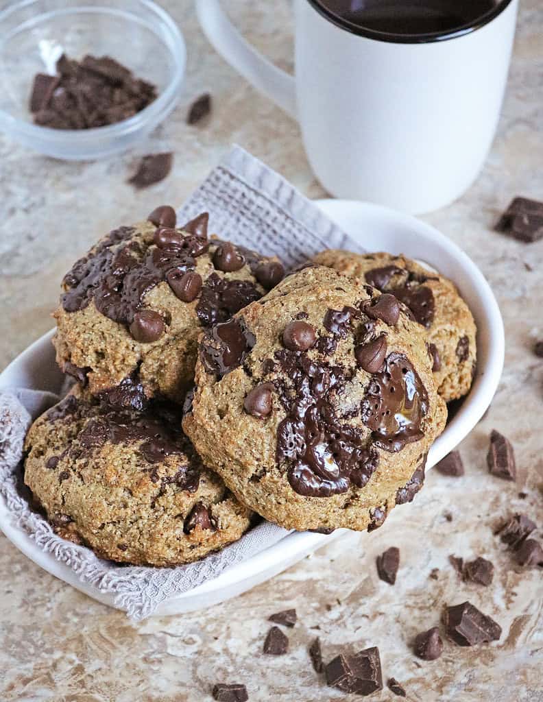 Brown Butter Rye Chocolate Chip Muffin Tops in a white bowl with a cup of coffee in the background.