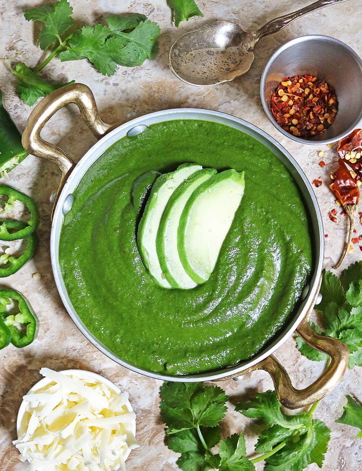 Delicious creamed spinach with harissa in a gold pan with parsley and chili flakes around it.