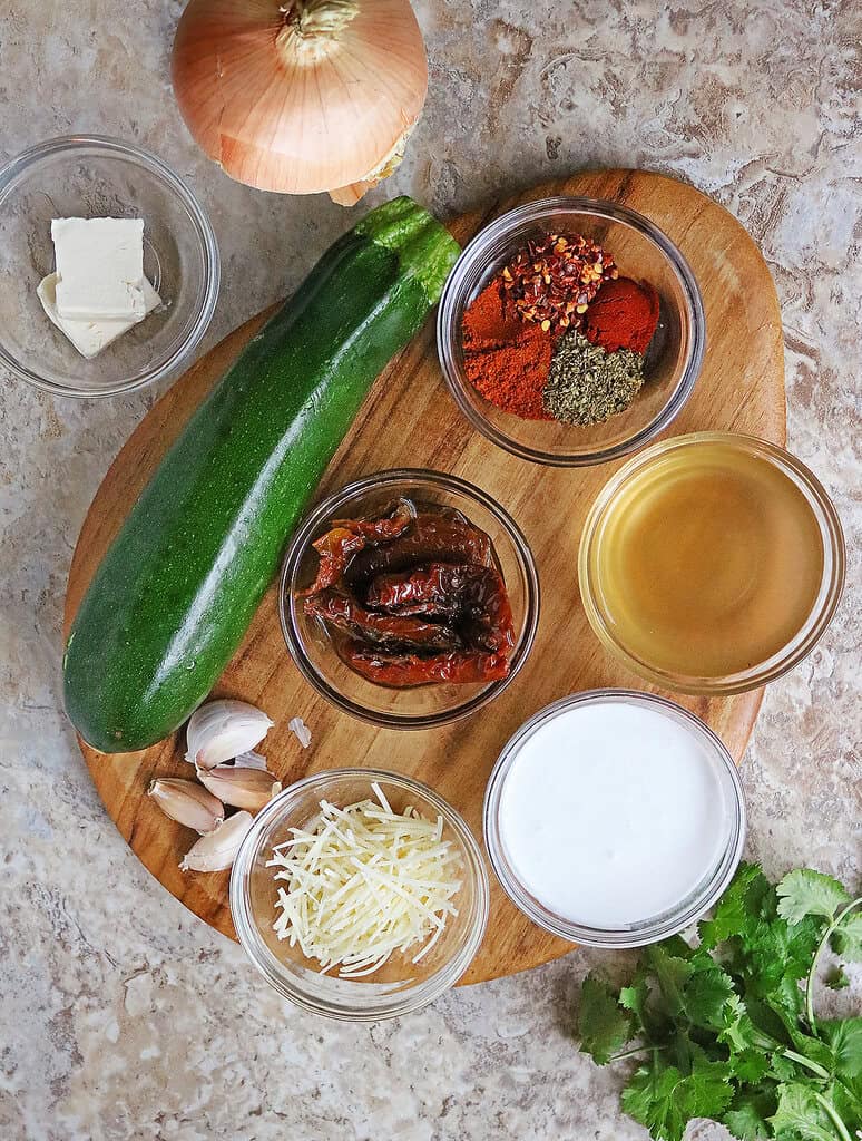 An overhead view of the Ingredients needed to make marry me zucchini on a cutting board.