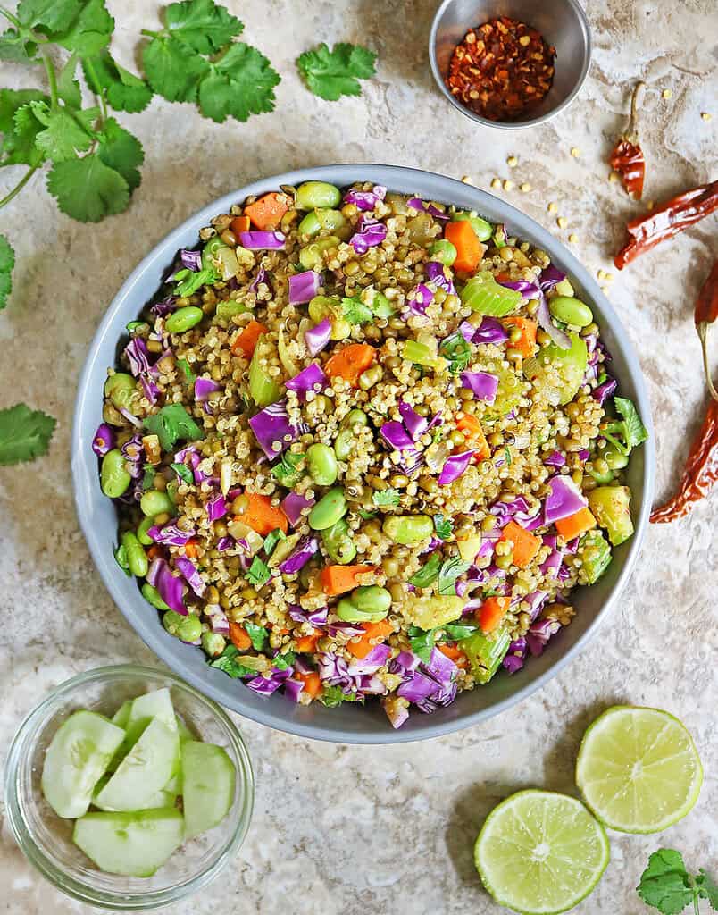 Overhead view of Moong Bean Quinoa and Vegetables in a bowl with cucumber and limes near.