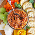Easy delicious pumpkin chutney in a glass jar on a platter with cheese, crackers and fruit.