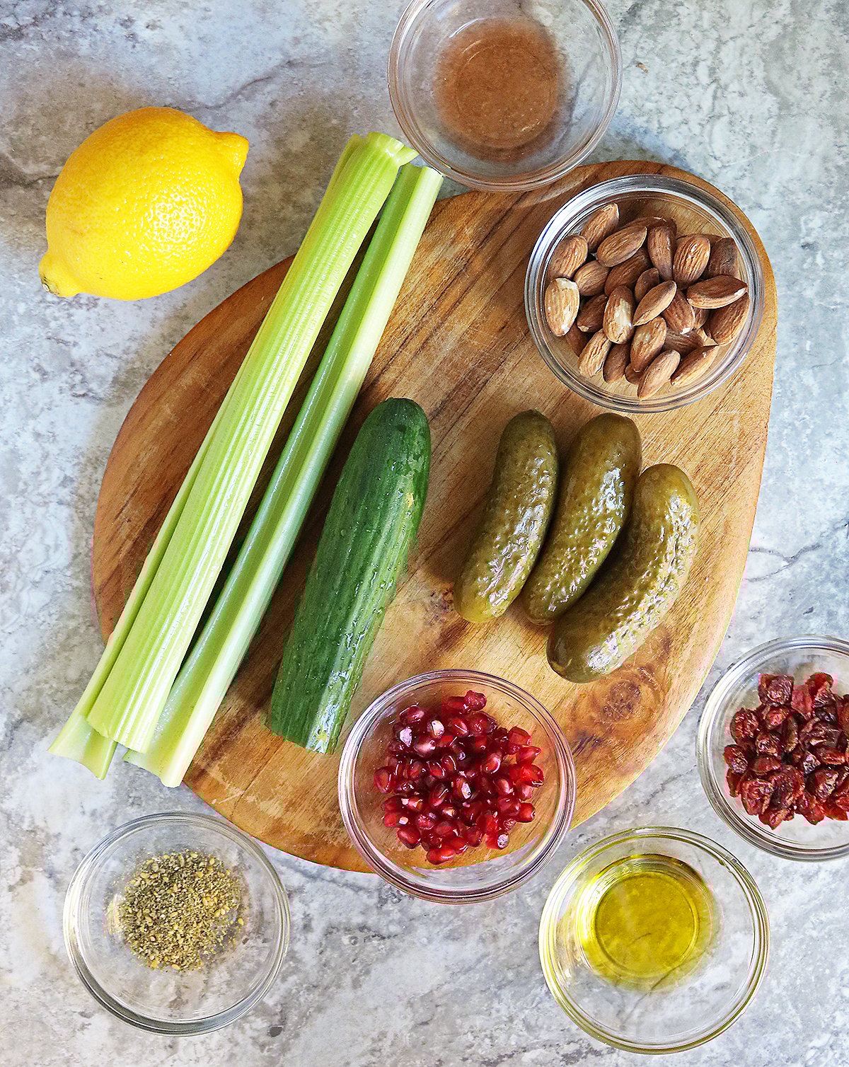10 Ingredients needed to make this pickle salad on a brown cutting board on a white and gray marble counter.