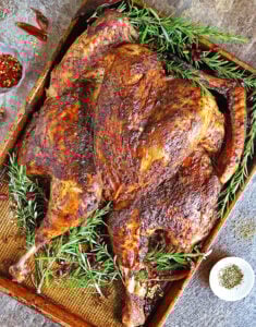 Spatchcock turkey with yogurt and spices on rimmed baking tray.