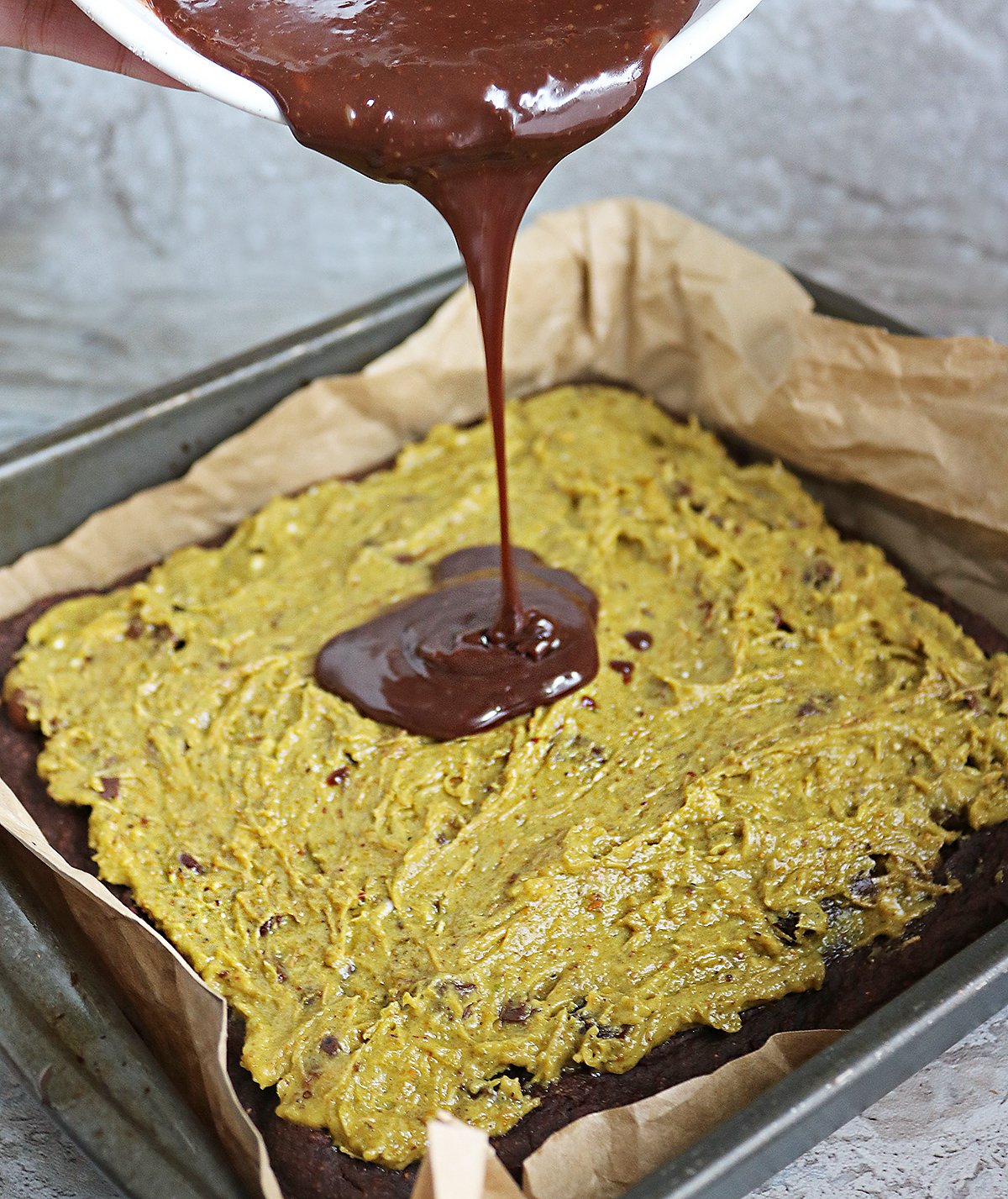Adding dairy-free chocolate ganache on top of pistachio layer.