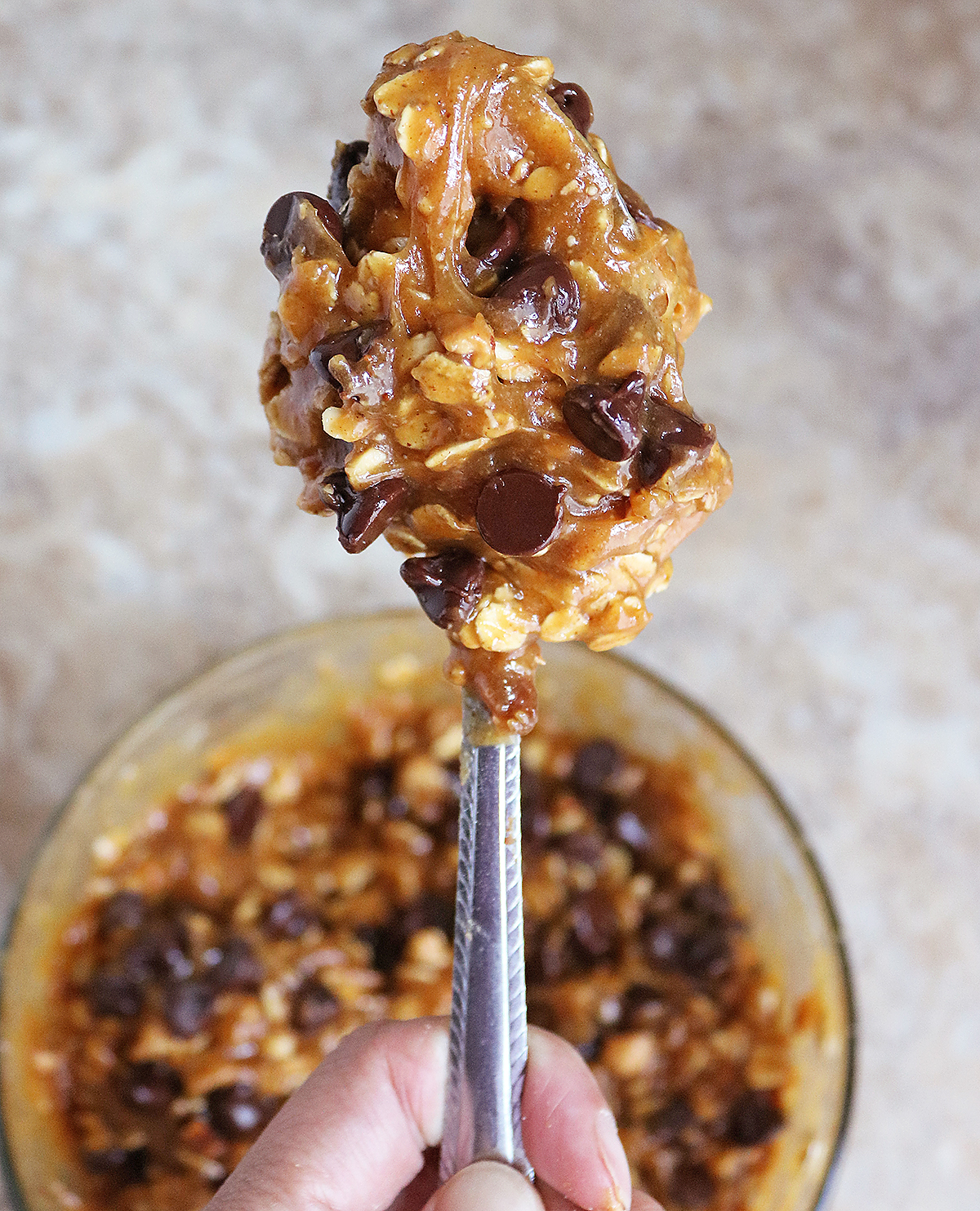 Close-up on a cookie dough ball with chocolate chips, held with a fork above a bowl of cookie dough.