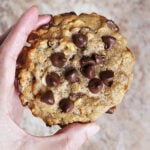 Close-up of a flourless collagen peanut butter chocolate cookie with melting chocolate chips in a hand
